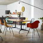 Clérachic swing-arm wall light above a dining area with an oval table, moulded chairs in orange, teal and yellow, and a round clock.