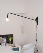 Clérachic black swing-arm wall light with a lit bulb above a small table with yellow flowers and a white chair.