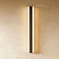 A tall black aluminium column sconce glows warm along both edges against a plaster wall in this Clérachic hero shot.