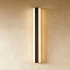 A tall black aluminium column sconce glows warm along both edges against a plaster wall in this Clérachic hero shot.