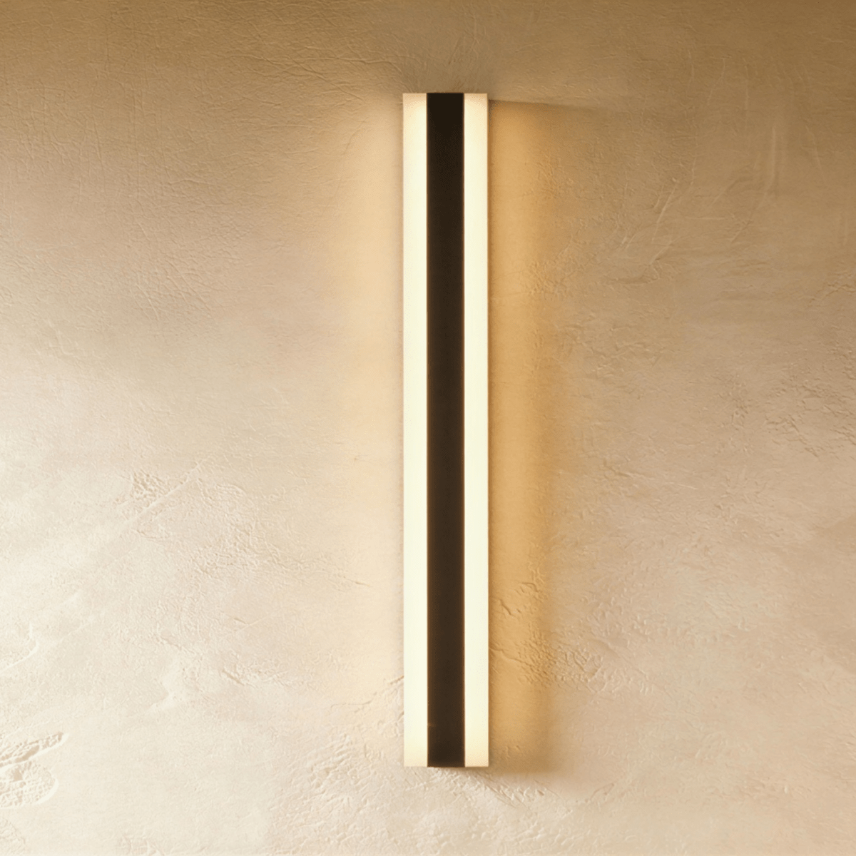 Seen from a slightly closer angle, the black aluminium column sconce lights a plaster wall evenly top to bottom, Clérachic hero shot.