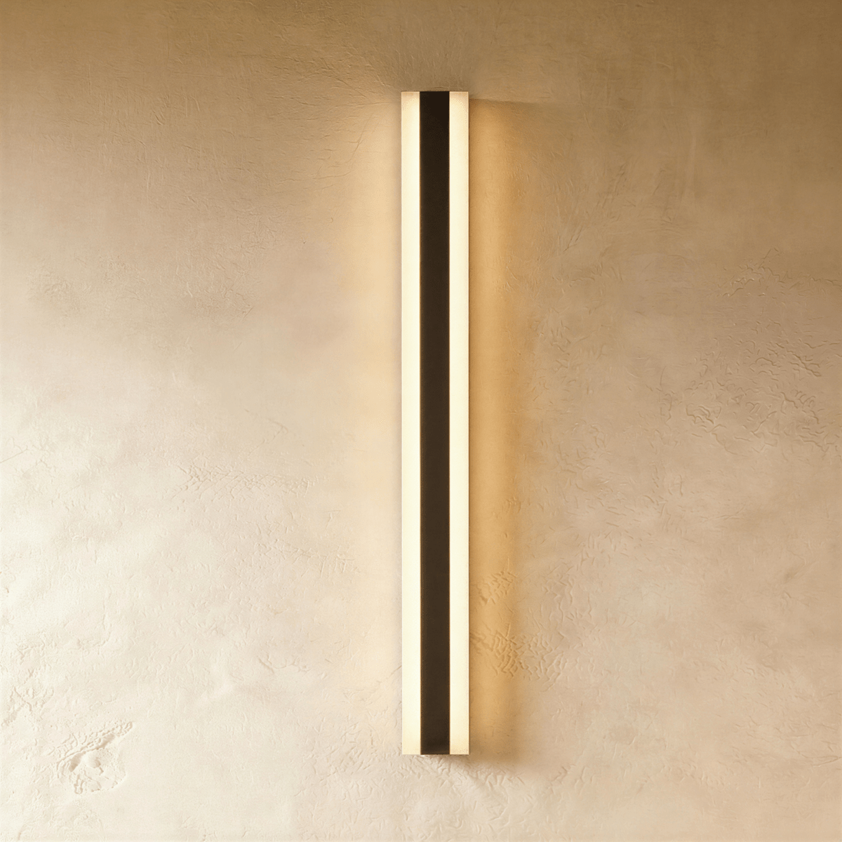 A further hero angle captures the black aluminium column sconce's full length glowing warm on plaster, Clérachic studio shot.