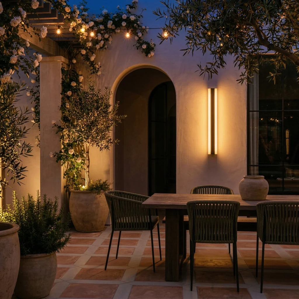 At dusk, the same black column sconce glows warm beside the pergola and string lights over the patio table, Clérachic lifestyle shot.