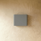 The same grey up-down sconce is shown unlit, its softly curved rectangular body set against plaster, Clérachic hero shot.
