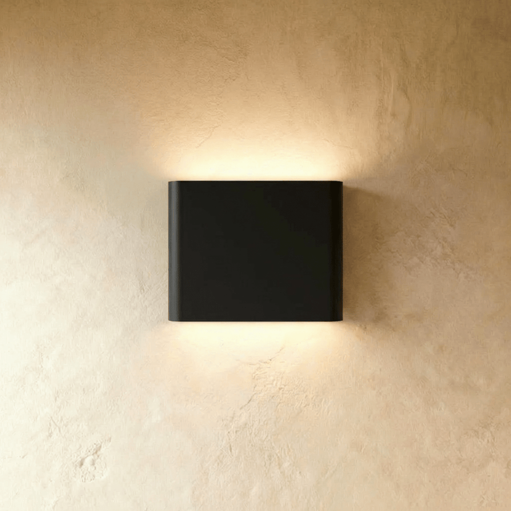 A black up-down wall sconce casts warm light both ways from its compact rectangular body, Clérachic hero shot.