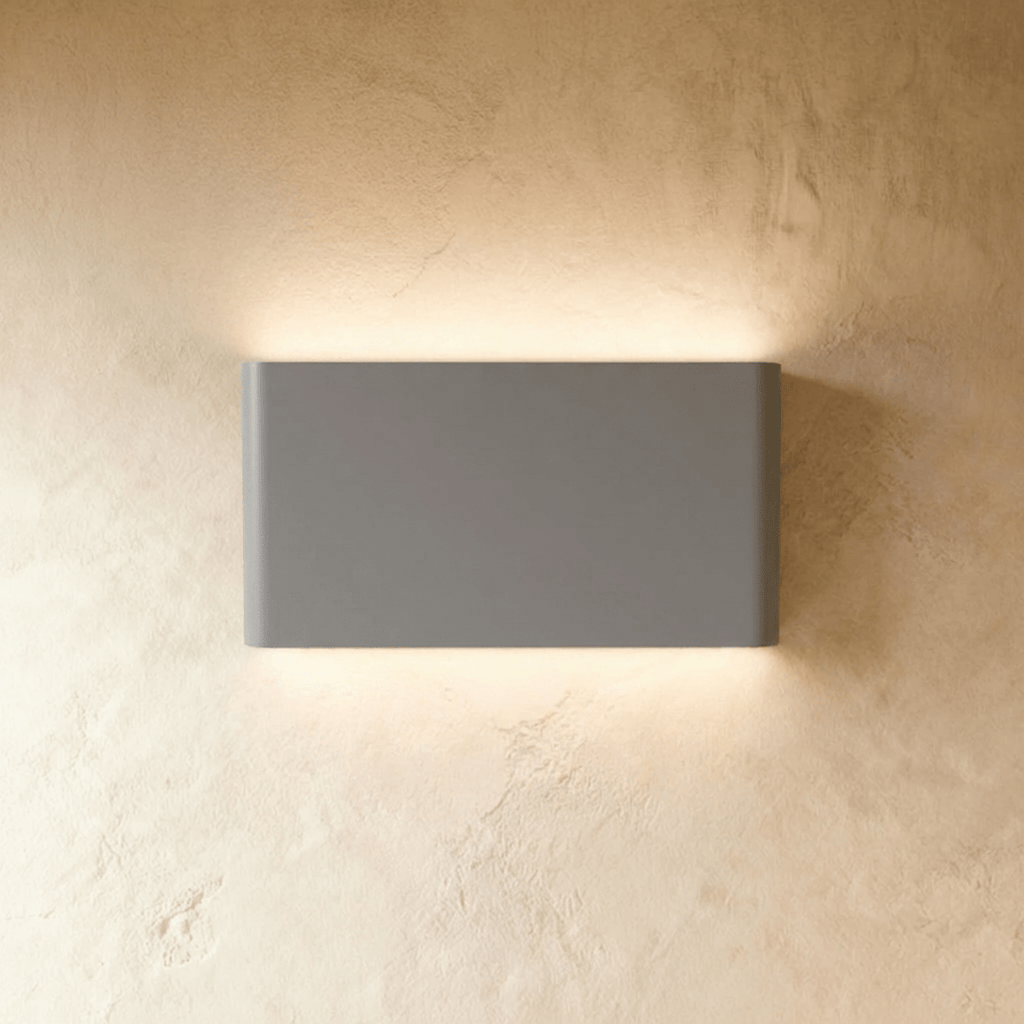 A mid-size grey up-down sconce spreads warm light across a wider stretch of plaster wall, Clérachic hero shot.