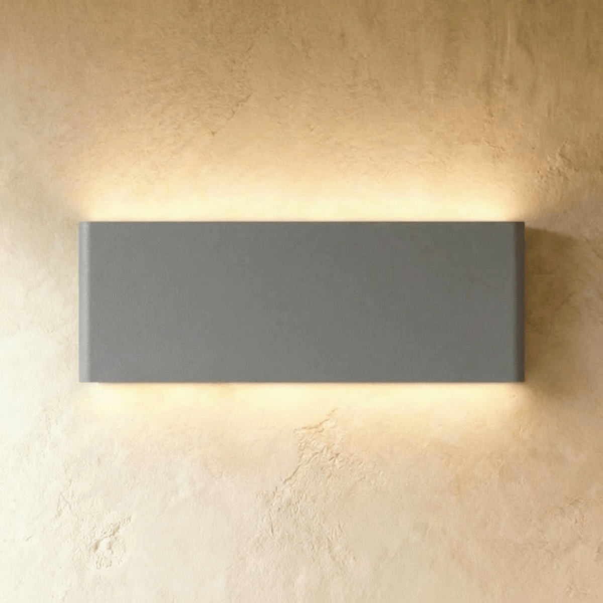 The largest grey up-down sconce spans a broad rectangular body, glowing warm top and bottom, Clérachic hero shot.
