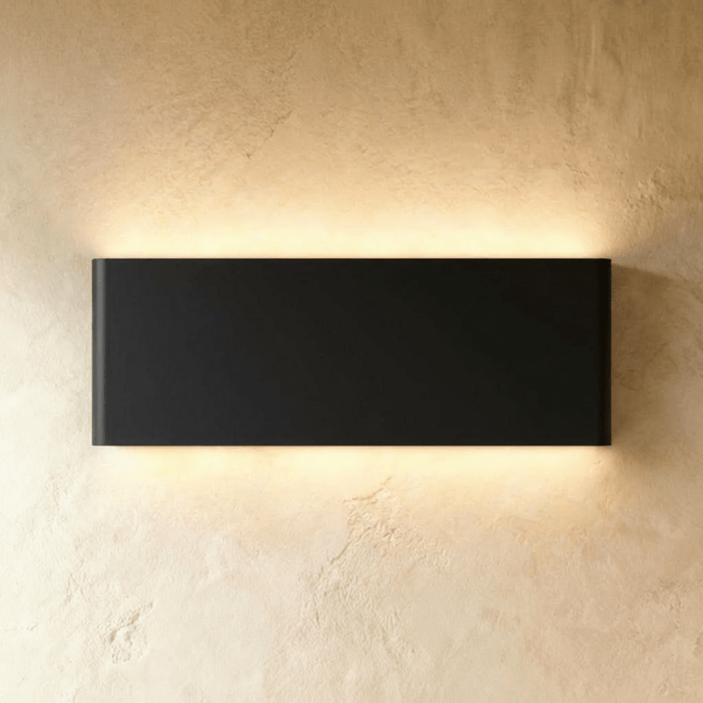 The largest black up-down sconce casts an even warm glow from its long rectangular body, Clérachic hero shot.