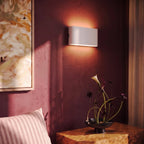 A closer crop shows the white sconce glowing beside an abstract painting and a calla lily arrangement, Clérachic lifestyle shot.
