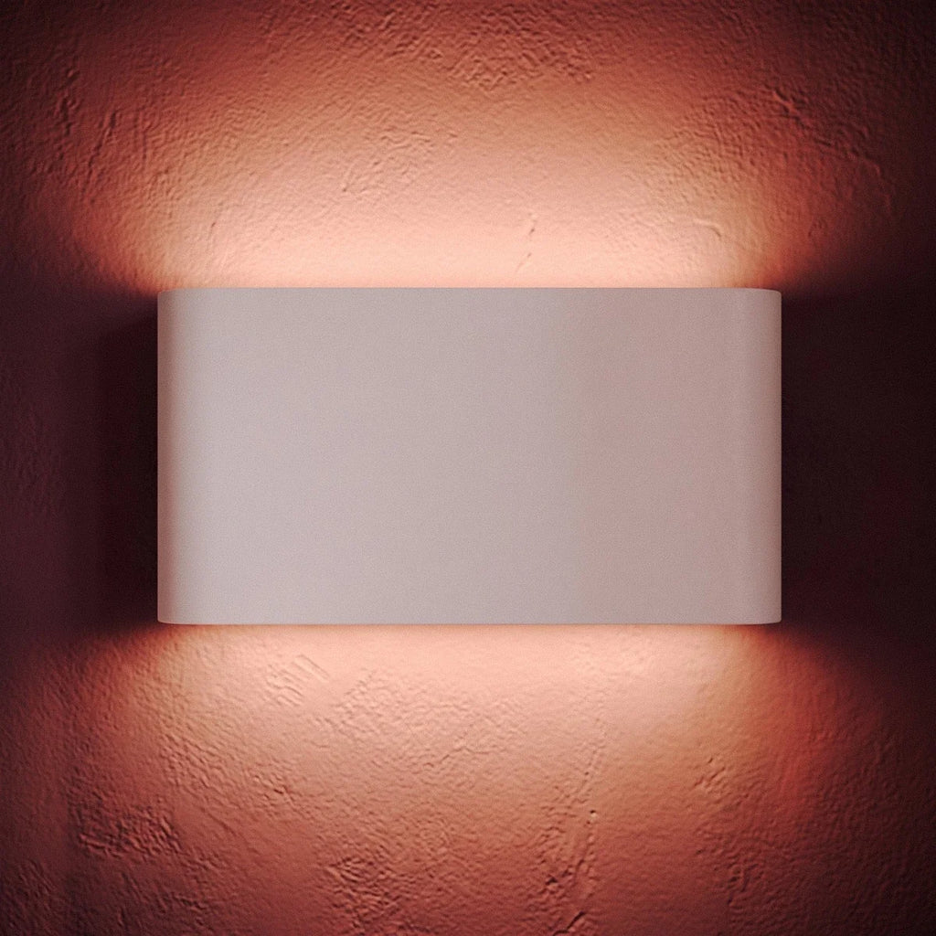 A tight crop on the lit white sconce shows its warm glow washing the rose-toned plaster wall, Clérachic detail shot.