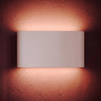 A tight crop on the lit white sconce shows its warm glow washing the rose-toned plaster wall, Clérachic detail shot.