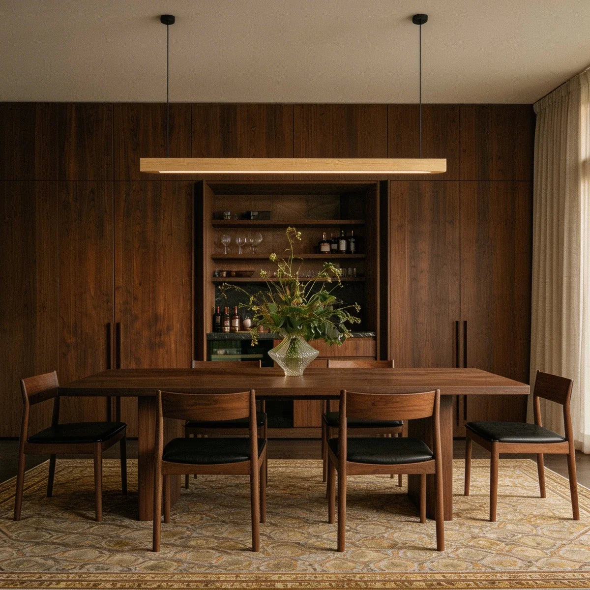 A Clérachic pine pendant bar lights a walnut-paneled dining room with a stocked bar cabinet behind it.