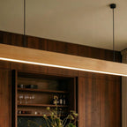 A close view shows the Clérachic pine pendant bar glowing above a walnut bar cabinet with glassware.