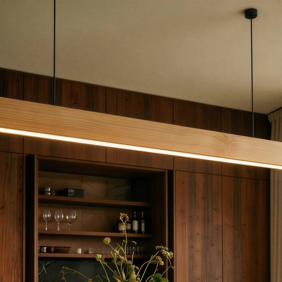 A close view shows the Clérachic pine pendant bar glowing above a walnut bar cabinet with glassware.