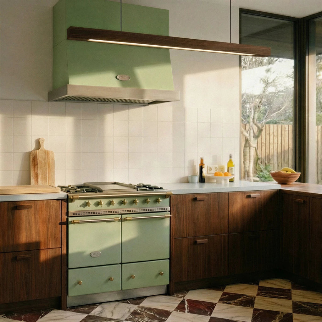 A Clérachic black walnut pendant bar glows warmly above a sage green range hood in this kitchen scene.