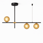 Clérachic 3-head linear chandelier lit, its amber glass globes glowing around the filament bulbs on a black bar.