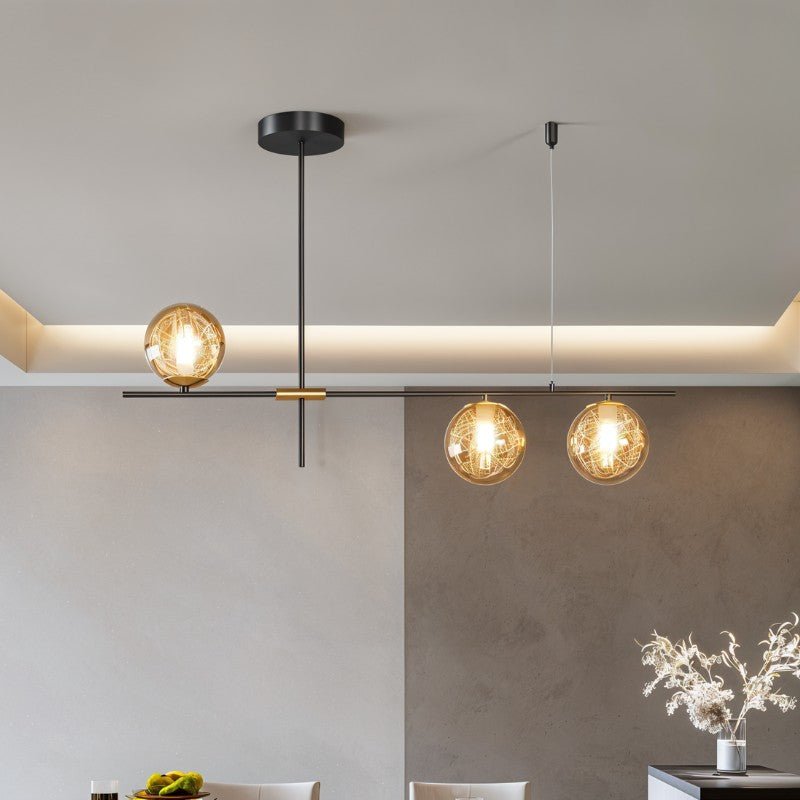 Clérachic 3-head chandelier with amber globes on a black bar above a dining area with a lit ceiling cove.