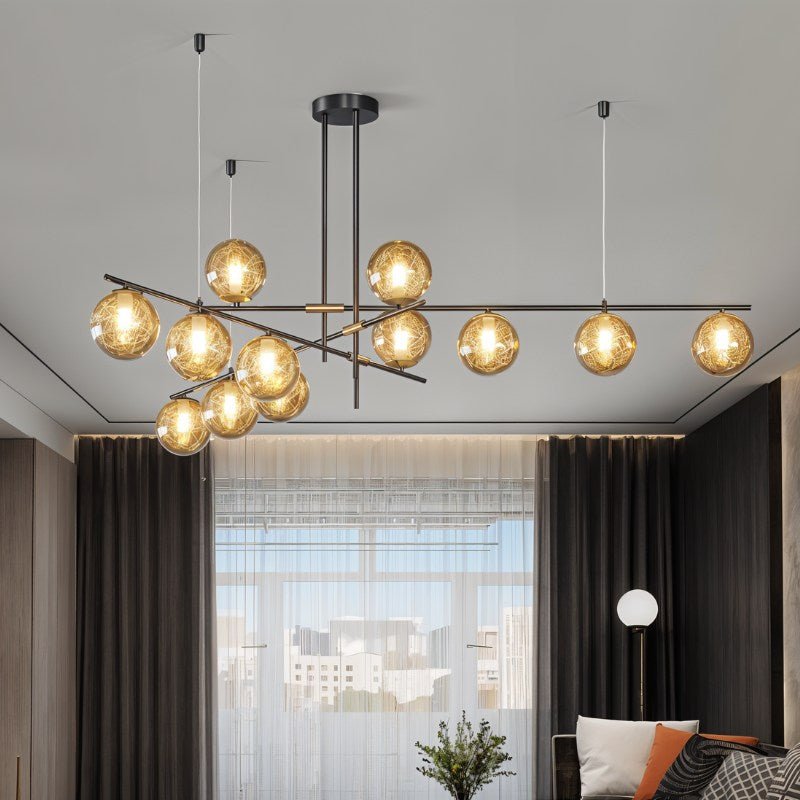 Clérachic 12-head chandelier with amber globes on crossed black bars, hanging in a living room by dark curtains.