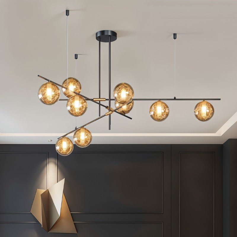 Clérachic 9-head chandelier with amber globes on angled black bars, lit in front of dark panelled walls.