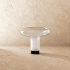 Clérachic mushroom-shaped blown-glass table lamp with a wide clear dish top and frosted white stem, unlit on a limewash backdrop.