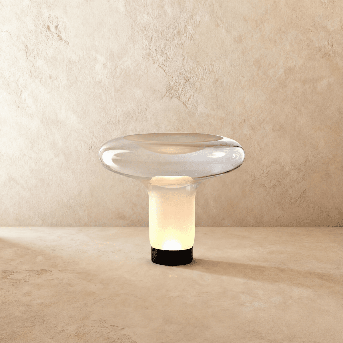 Clérachic mushroom-shaped glass table lamp lit warm inside its frosted white stem, with a clear dish top and black base.