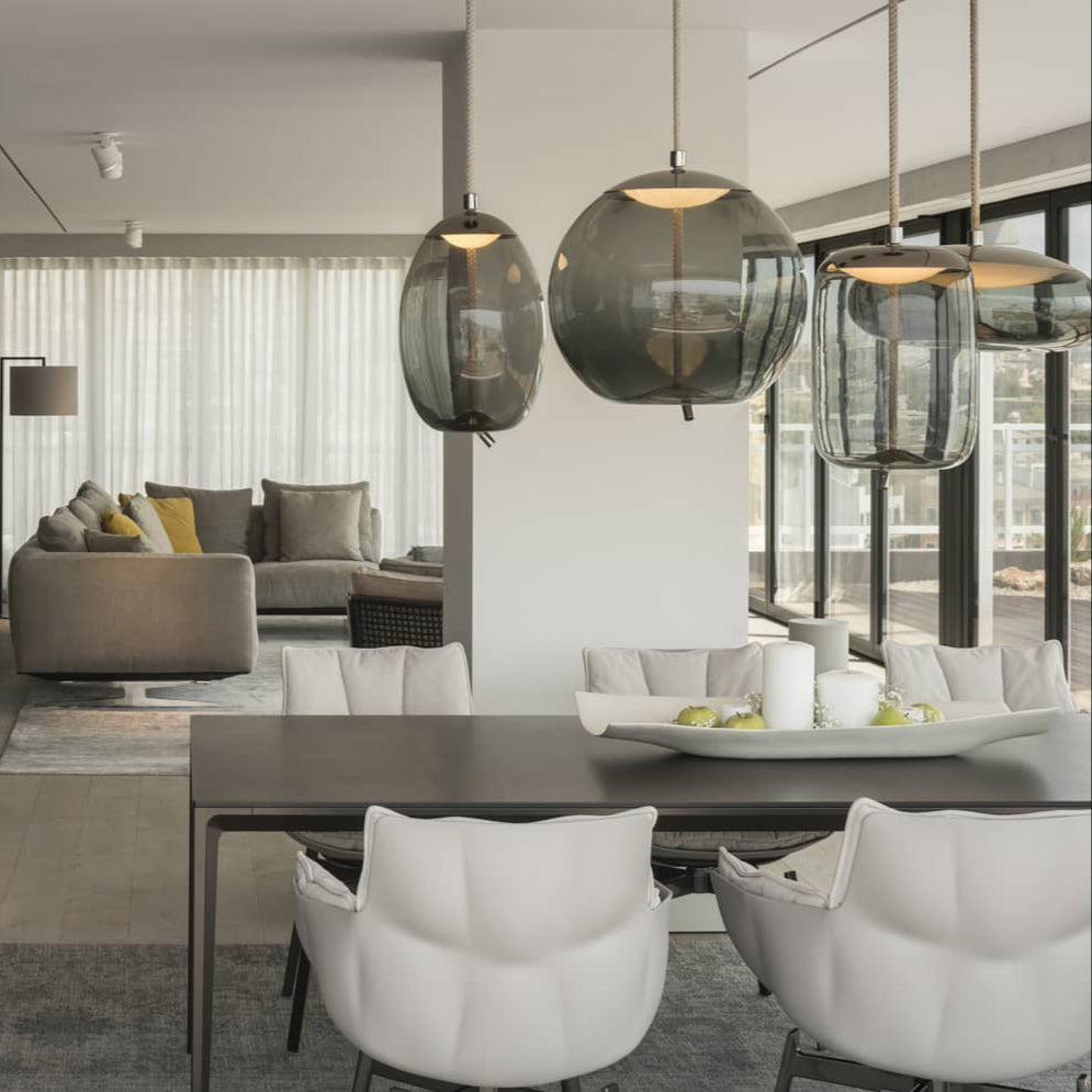 Smoke-grey glass Clérachic pendants in round and tall shapes hang above a dark dining table with white upholstered chairs.