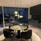 Lit at dusk, a round glass Clérachic pendant and two smaller ones hang above a round marble-topped table with dark leather armchairs.