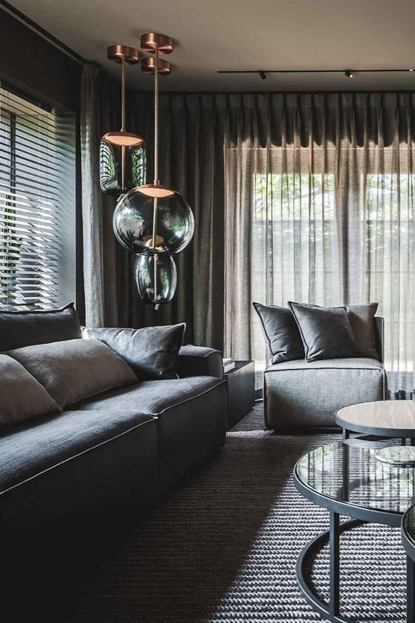 Smoke-grey glass Clérachic pendants hang from copper-toned canopies in a dark living room with heavy curtains and a leather sofa.