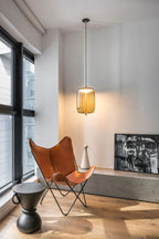 A single amber glass Clérachic pendant glows beside tall windows, above a leather butterfly chair and a small stone ledge.