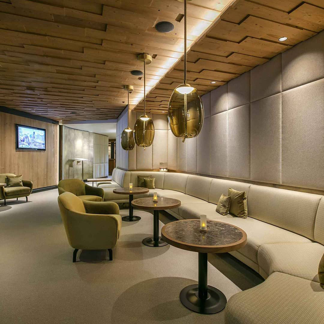A line of amber glass Clérachic pendants hangs along a timber-ceilinged lounge with round tables, velvet armchairs and a curved banquette.