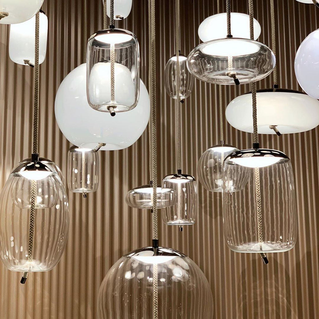 Close view of clear glass and white opal Clérachic pendants in different shapes, hanging together against a ribbed wooden wall.