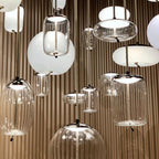 Close view of clear glass and white opal Clérachic pendants in different shapes, hanging together against a ribbed wooden wall.