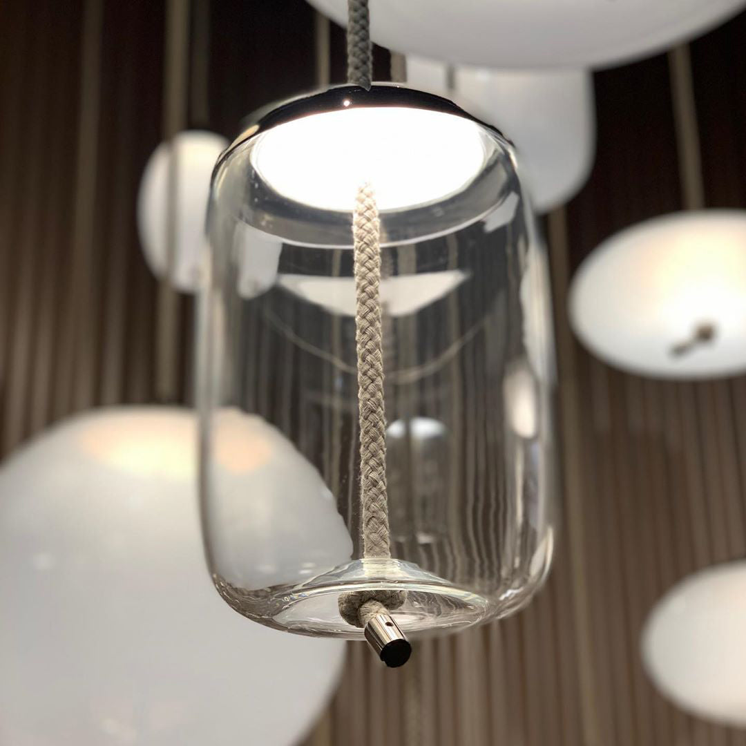 Close view of a clear glass Clérachic pendant with a braided rope running through it, surrounded by round white opal pendants.