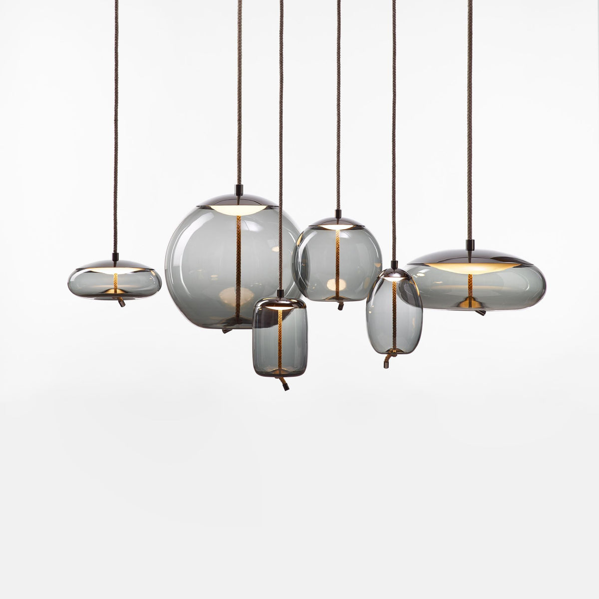 On a white backdrop, six smoke-grey glass Clérachic pendants in round, flat and tall shapes hang at different heights from braided cords.