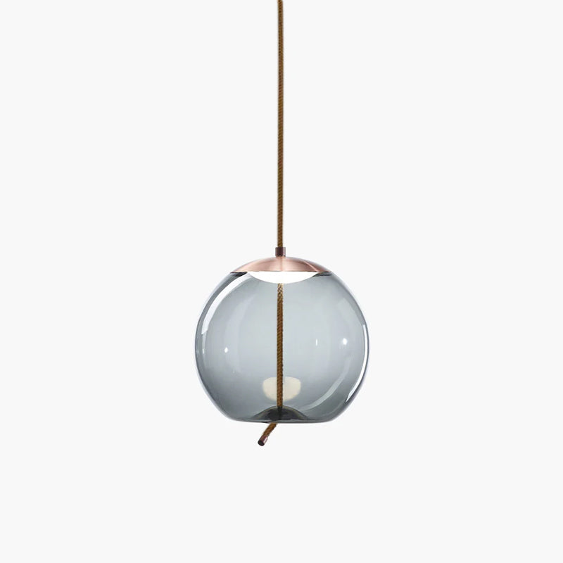 A round smoke-grey glass Clérachic pendant with a copper-toned cap hangs from a braided cord on a plain white backdrop.