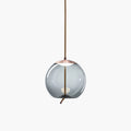 A round smoke-grey glass Clérachic pendant with a copper-toned cap hangs from a braided cord on a plain white backdrop.