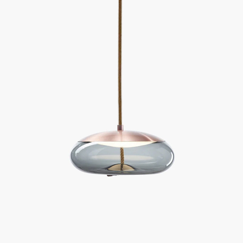 A flat, wide smoke-grey glass Clérachic pendant with a copper-toned top hangs from a braided cord on a pale backdrop.