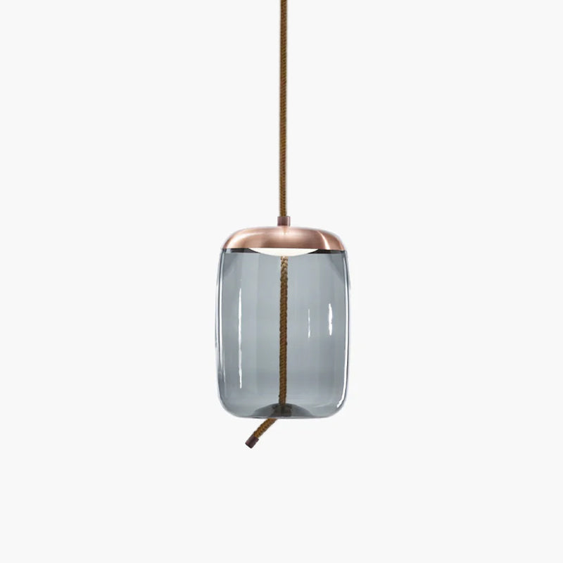 A tall, rounded-cylinder smoke-grey glass Clérachic pendant with a copper-toned cap hangs from a rope cord on a pale backdrop.