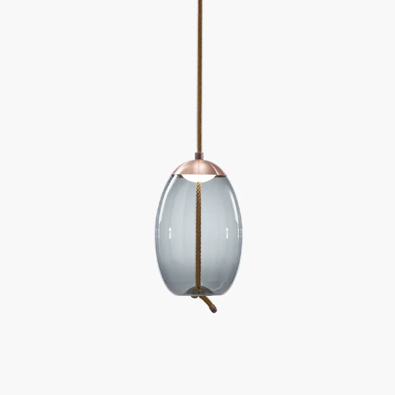 A narrow oval smoke-grey glass Clérachic pendant with a copper-toned cap hangs from a braided cord on a pale backdrop.