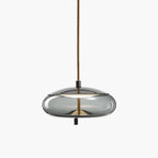 A wide, flat smoke-grey glass Clérachic pendant with a dark metal top hangs from a brown braided cord on a pale backdrop.