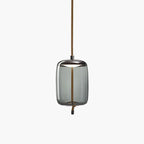 A tall smoke-grey glass Clérachic pendant with a dark metal cap and a knotted rope tail hangs on a pale backdrop.