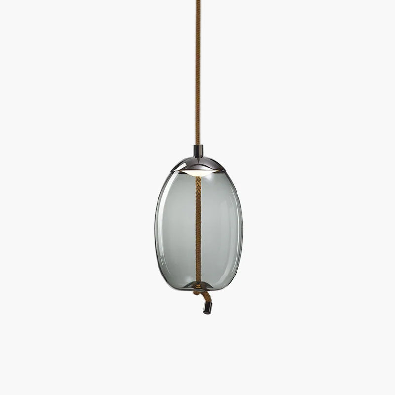 A narrow oval smoke-grey glass Clérachic pendant with a dark cap hangs from a brown braided cord on a pale backdrop.