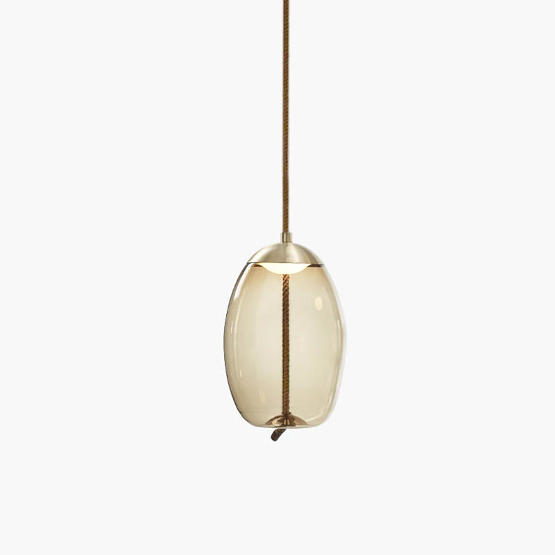 A small oval amber glass Clérachic pendant with a brass-toned cap and braided cord hangs on a pale backdrop.