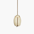A small oval amber glass Clérachic pendant with a brass-toned cap and braided cord hangs on a pale backdrop.
