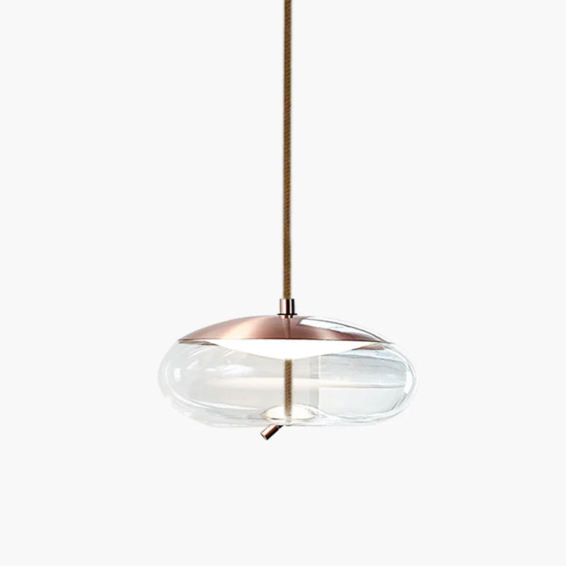 A flat, wide clear glass Clérachic pendant with a copper-toned top hangs from a braided cord on a pale backdrop.
