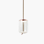 A tall clear glass Clérachic pendant with a copper-toned cap and a rope tail hangs on a pale backdrop.