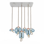 Six aqua-blue glass Clérachic pendants in round, flat and tall shapes hang from one long white ceiling plate on a pale backdrop.
