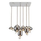 Six smoke-grey glass Clérachic pendants in mixed shapes hang from one long white ceiling plate, each lit softly from inside.