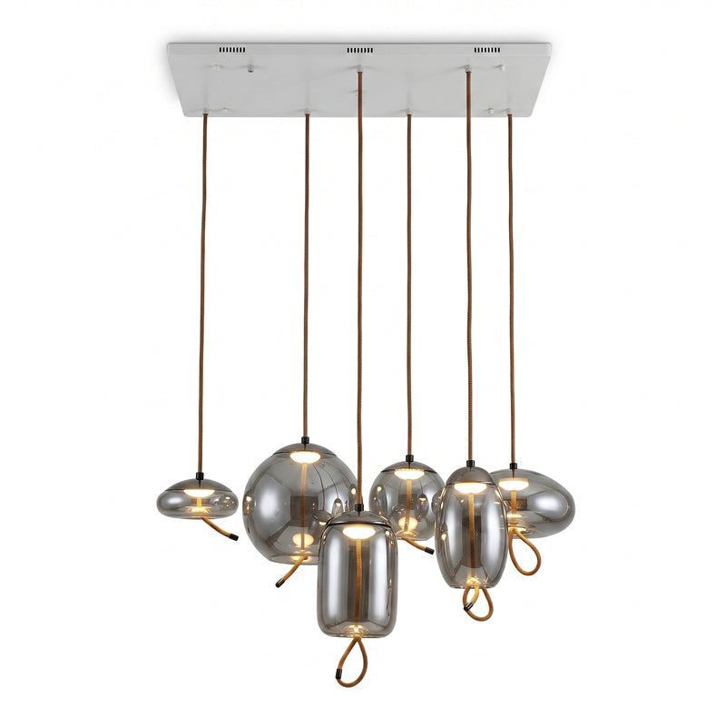 Six smoke-grey glass Clérachic pendants in mixed shapes hang from one long white ceiling plate, each lit softly from inside.