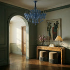 Clérachic blue crystal chandelier in a panelled hallway with an arched doorway, a burr wood console and two fringed stools